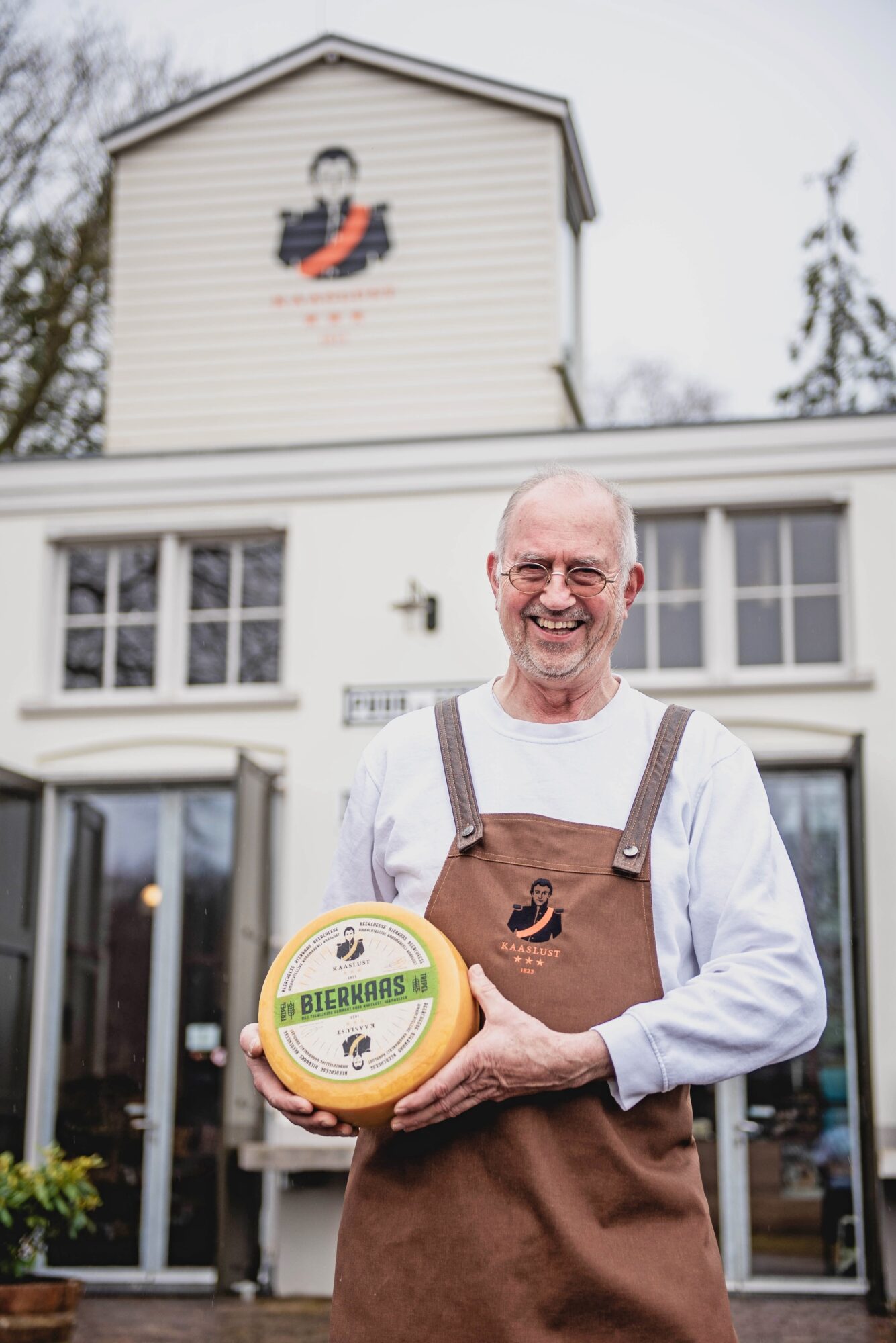 Jan Craens met een kaas in zijn hand voor een gebouw.